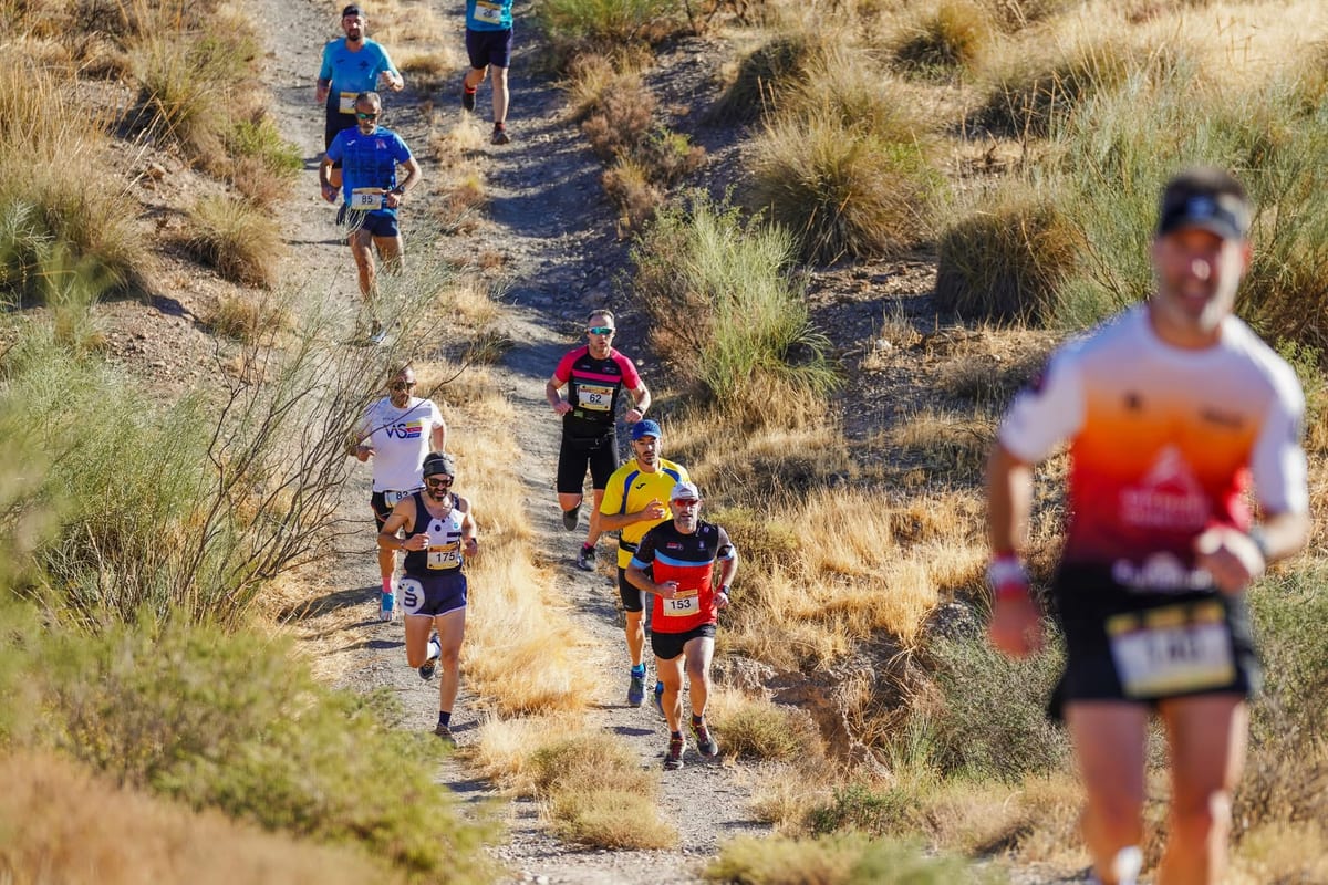 Una fila de participantes baja por una senda estrecha entre retamas y esparto