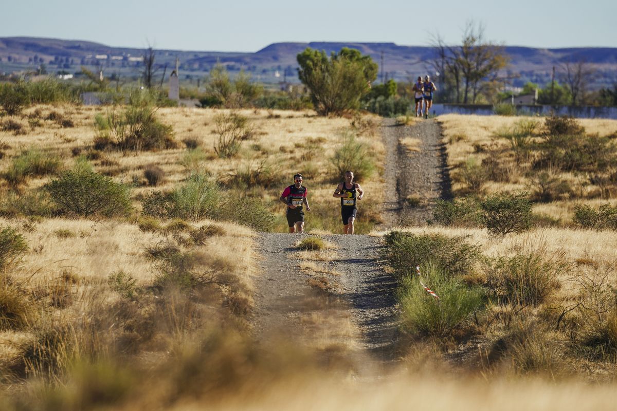 Dos corredores emparejados en la pista de tierra, con Tabernas a lo lejos